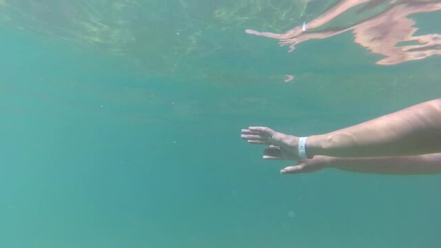 Underwater view of female hands of happy woman enjoying warm sea water during summer beach vacations. Video shoot by action camera