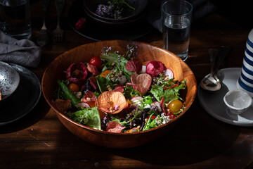 Healthy appetizing colorful salad with various fresh vegetables and herbs garnished with edible flowers served in wooden bowl on table setting for dinner