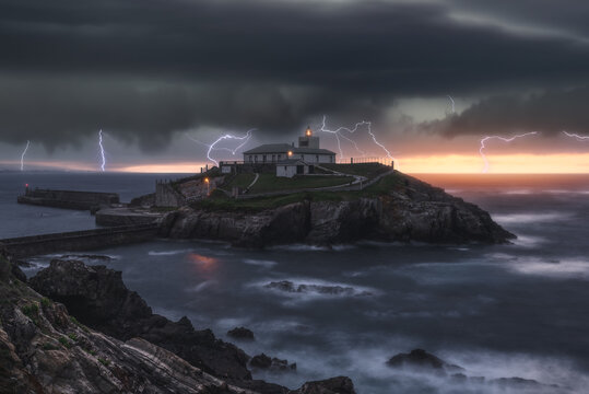 Picturesque view of thunderstorm with flashes of lightnings above lonely house on island in stormy sea at sunset
