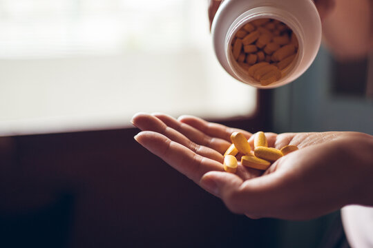 Side view of crop anonymous female putting yellow vitamin pills from plastic bottle into hand
