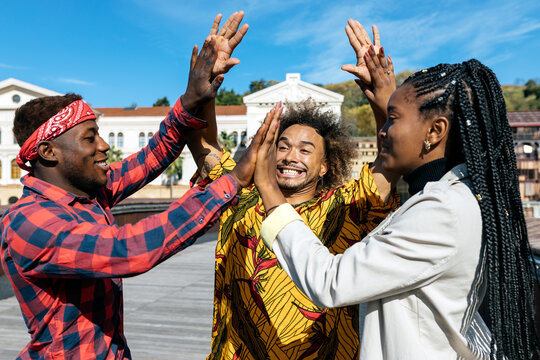 Group of excited optimistic young black students having fun and giving high five to each other while having meeting on urban square