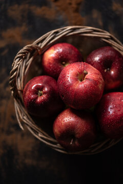 Top view of pile of wet red apples placed in wicker basket on rustic table