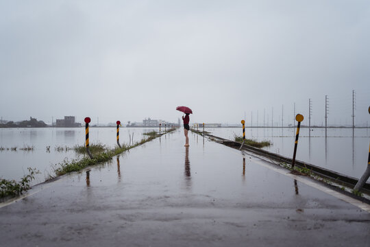 Side view of faceless female with umbrella walking barefoot along wet empty road on rainy day under cloudy sky in Yilan County