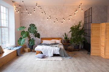 Cozy bedroom area at luxury studio apartment with a free layout in a loft style with big panoramic window and green plant.