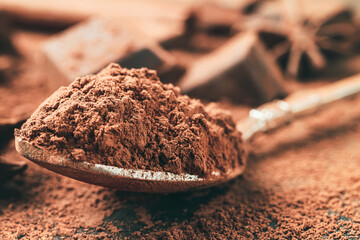 Brown cocoa powder in the spoon, chopped chocolate cubes on dark background, close-up view