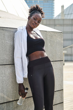 Relaxed African American female runner standing on the street in city holding bottle of fresh water during training