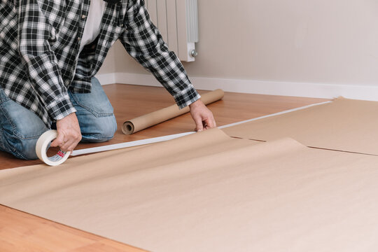 Unrecognizable male painter sticking craft paper to floor with tape while preparing modern room for painting and renovation