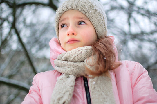 Little upset girl is wearing pink clothes in the park and crying. Unhappy kid got frozen spending time outdoors during cold winter
