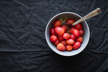 Top view of bowl full of marinated red grape tomatoes with spoon placed on black surface