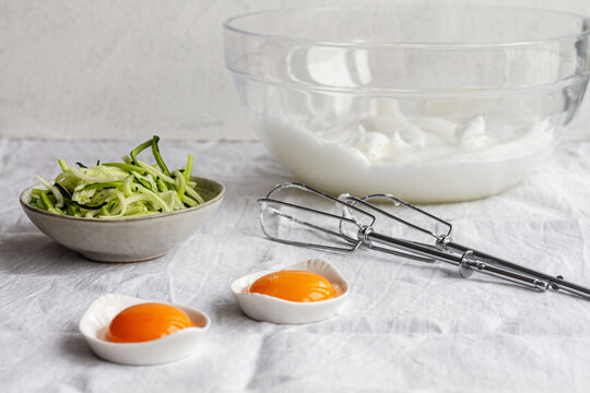 Whole egg yolks and whipped egg whites with chopped green vegetables prepared for cooking process on kitchen table