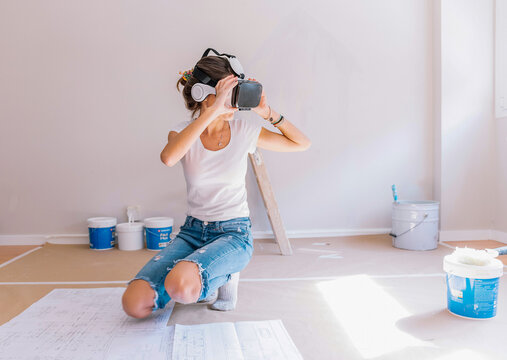 Young woman in VR headset gesticulating while visualizing apartment plan in cyberspace during renovation at home