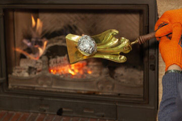 Potato in foil lies on spatula in front of fireplace