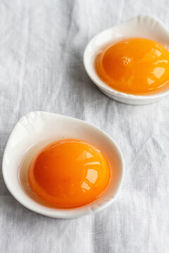 High angle of small white bowls with uncooked egg yolks placed on white tablecloth in kitchen