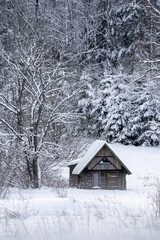 a little gray wooden house stands on a hillside forest in the winter white fluffy snow