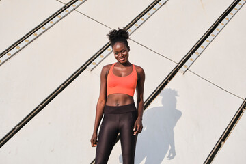 Smiling African American female athlete in sportswear standing in urban area in city looking at camera
