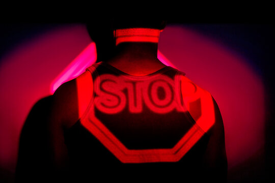 Side view of African American males standing in dark studio illuminated by red neon light of projection of stop road sign
