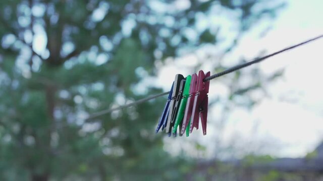 Multicolored clothes pins hangs on rope in village backyard outdoor against tree and sky.