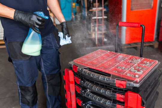 Unrecognizable male mechanic spraying tool box with detergent during work in professional garage