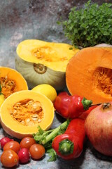 colorful vegetables, tomatoes, peppers, and large orange pumpkins cut in half, celery and fresh oregano in the background