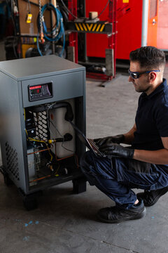 Adult man in goggles using laptop to program broken machine during work in modern workshop