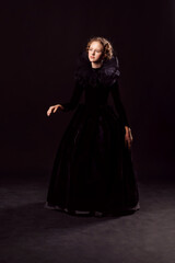 Fototapeta premium Beautiful little red-haired girl in a medieval queen costume. Black on black. Stylization.