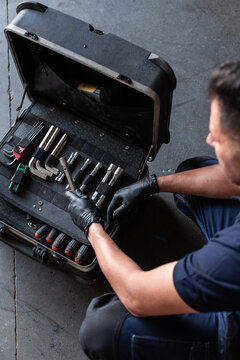 From above male technician picking screwdriver bits from tool box while working in garage