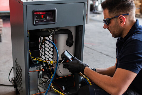 Male mechanic in goggles and gloves using voltage tester on modern machine during work in workshop