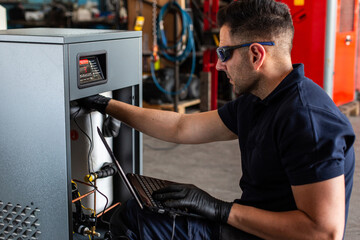 Adult man in goggles using laptop to program broken machine during work in modern workshop