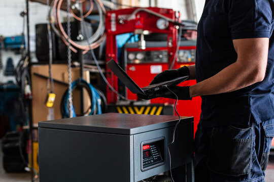 Unrecognizable adult man in using laptop to program broken machine during work in modern workshop