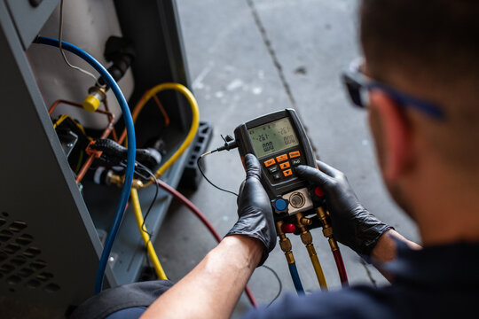 Male mechanic in goggles and gloves using voltage tester on modern machine during work in workshop
