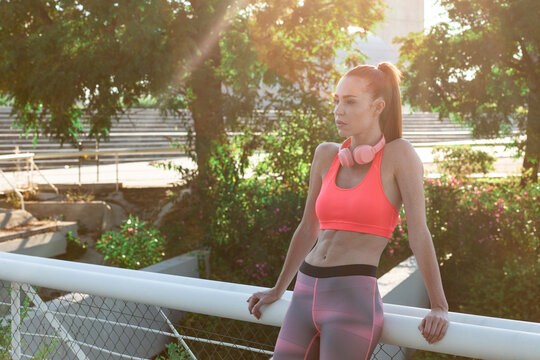 Confident fit female runner standing on street in summer and having break during training in city while looking away