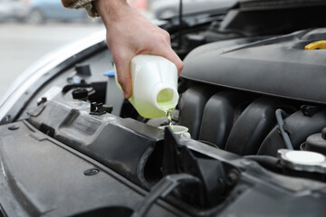 Man filling car radiator with antifreeze outdoors, closeup