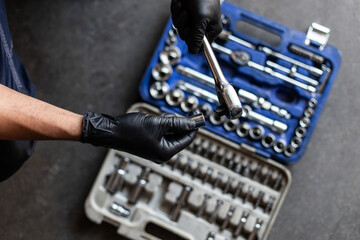 From above anonymous male technician in latex gloves selecting wrench bit from tool box during work in garage