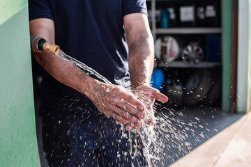 Crop anonymous male workman washing hands under tap with water after finishing work in repair service workshop