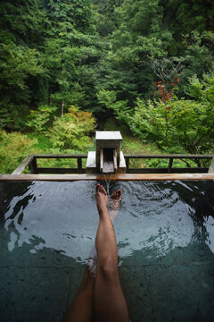 Legs and feet of caucasian female traveler enjoying a thermal waters bath in Japanese onsen, view from above