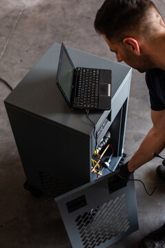 Adult man in using laptop to program broken machine during work in modern workshop