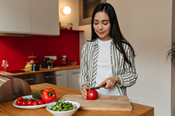 Lovely woman in striped shirt cuts tomato in kitchen
