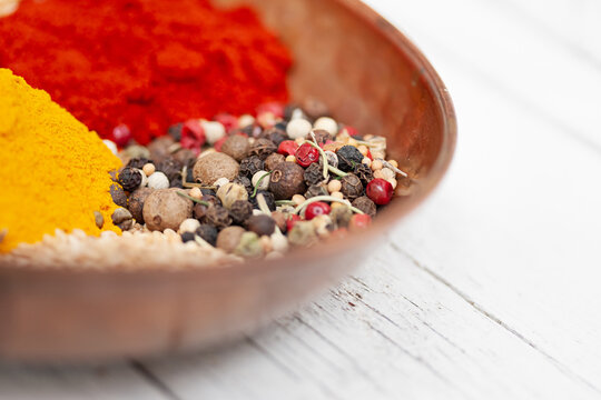 Closeup of bowl with assorted aromatic colorful spices including mix of peppercorns with paprika and turmeric powder placed on white wooden table