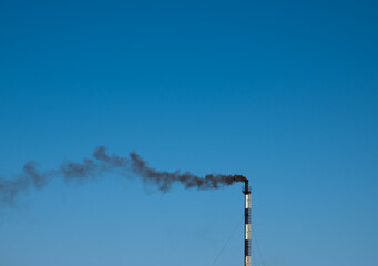 The chimney smokes black smoke against a blue sky.