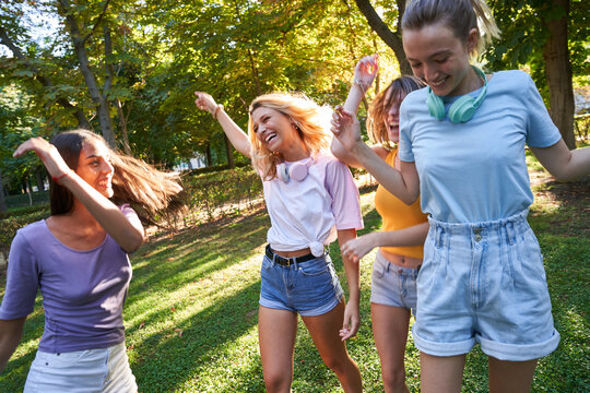 Group of laughing multiracial teen female friends having fun and dancing together while spending summer day in green park