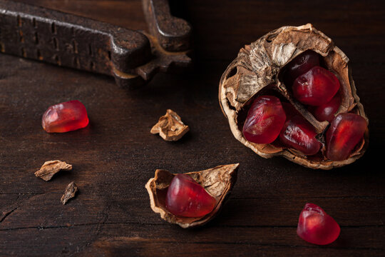 Top view still life composition with ripe red pomegranate seeds arranged in walnut shells on dark wooden background