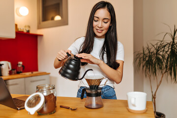 Beautiful long-haired girl poses in kitchen and pours coffee with boiling water