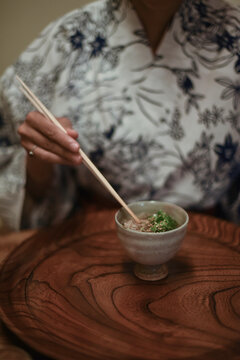 Close up view of hands of female caucasian woman in kimono using chopsticks to eat Japanese food at ryokan