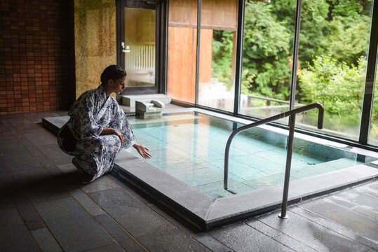 Young caucasian woman in a kimono touching thermal waters before enjoying a traditional bath at a Japanese onsen