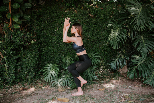 Side view of focused female in sportswear standing barefoot in Garudasana and practicing yoga in summer garden