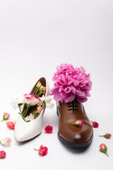 blooming peony flower in male shoe near female footwear on white