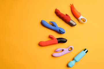 top view of six sex gadgets and a masturbation device on an orange background. Dildos or clitoral massagers. Flat lay and space for text