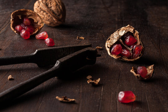 Still life composition with ripe red pomegranate seeds arranged in walnut shells on dark wooden background