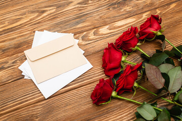 high angle view of red roses near envelopes and papers on wooden surface