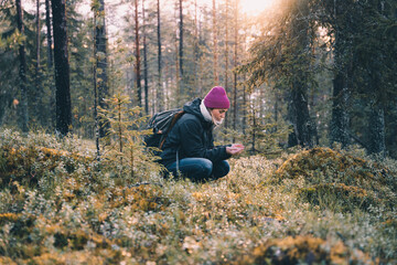 Side view of female explorer sitting in woods in cold season and looking at plants